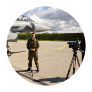 Christian Krieg als Presseoffizier im Feldanzug vor Kameras und Mikrofonen bei einer Pressekonferenz. Im Hintergrund ist ein Eurofighter der Luftwaffe zu erkennen
